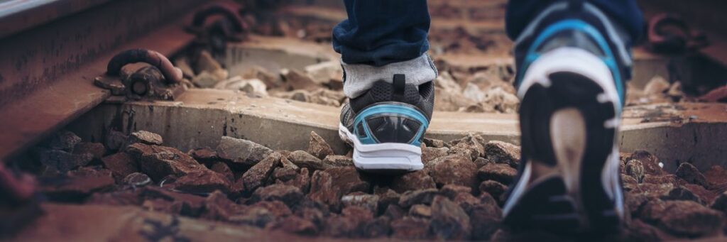 A person walking on rocky railway track wearing sports shoes, representing the health benefits of walking and daily physical activity.