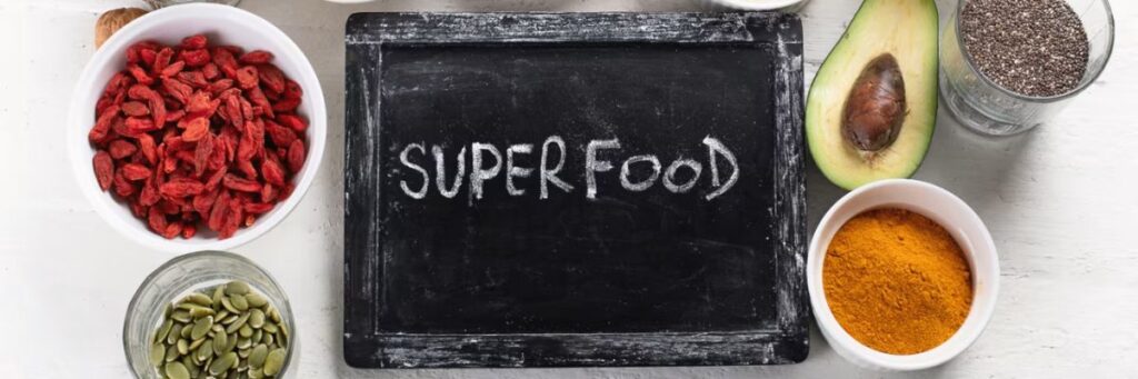 A top view of fat-burning superfoods including goji berries avocado chia seeds pumpkin seeds and turmeric placed around a chalkboard.