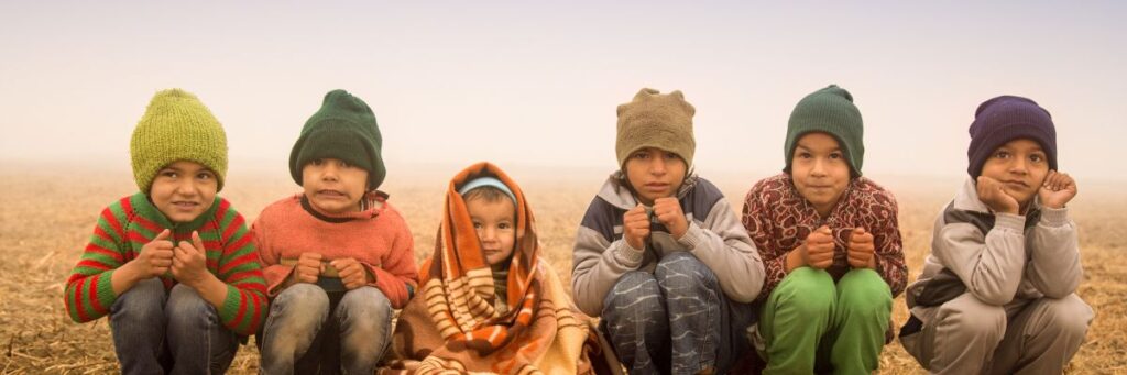 Children sitting outdoors in cold winter weather, highlighting the need for warm winter foods and nutrition.