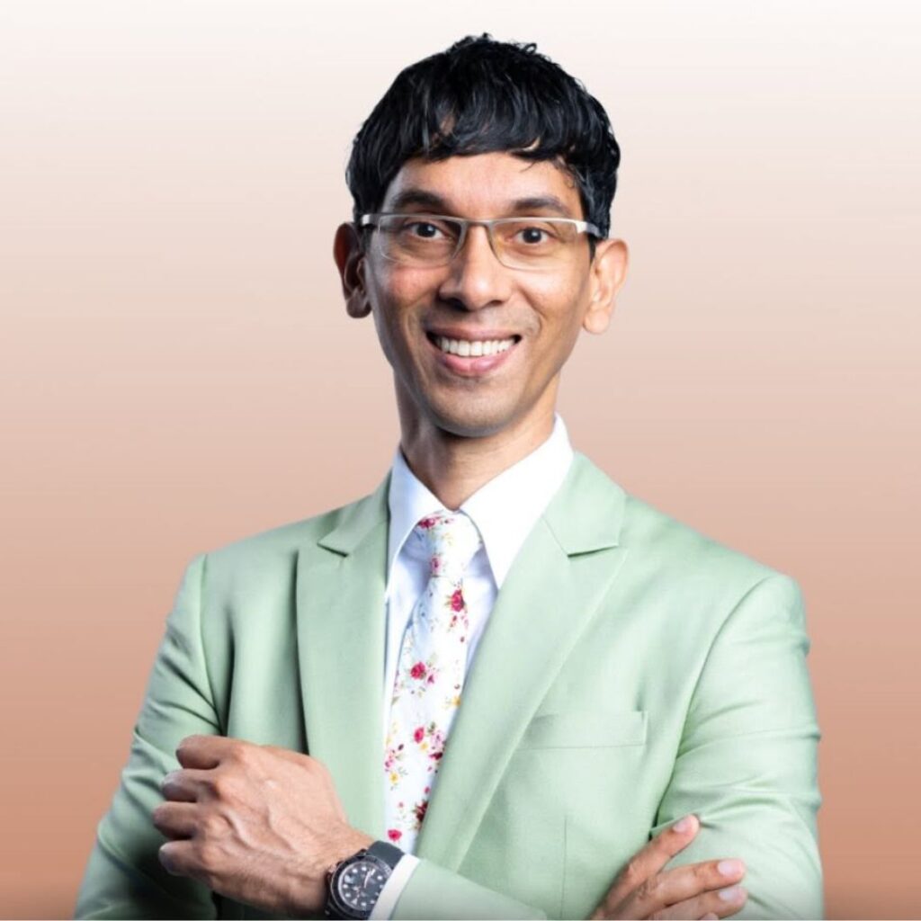 Ryan Fernando, famous dietitian in India, wearing a light green suit and floral tie with arms crossed against a soft gradient background, representing expert Indian sports nutrition.