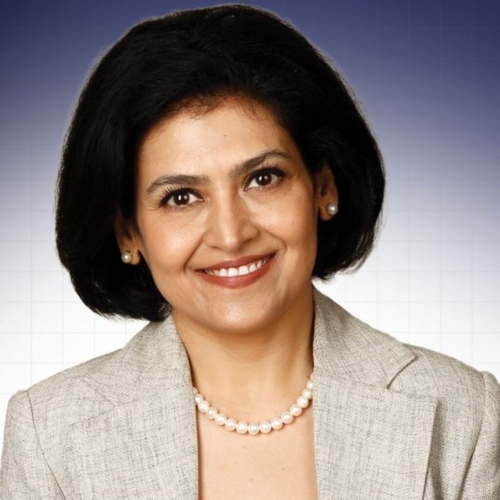 Shikha Sharma, famous dietitian in India, smiling professionally in a gray blazer with pearl necklace against a blue background, representing expert wellness and nutrition guidance.